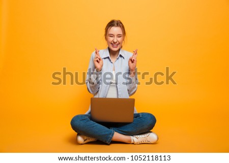 Image of cute young lady student sitting isolated over yellow background make hopeful gesture using laptop computer.