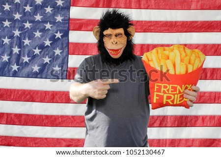 A man wears a Monkey or Chimpanzee mask while holding funny pillow props in a Photo Booth against an American Flag. Photo Booths are popular at Weddings and all parties and events. 