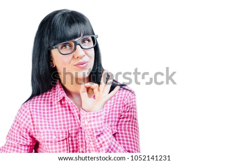 A positive funny brunette in a pink shirt shows an OK sign, demonstrates that everything is in order, agrees. Cheerful woman gestures indoors. Body language and human emotions