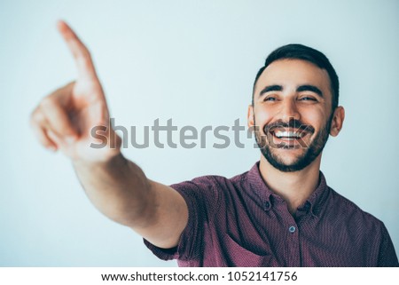 Closeup portrait of happy young handsome man pointing blurred finger at something out of view. Choice concept. Isolated front view on grey background.