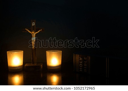 A cross with holy bible on a wooden table with a light candles. Low key concept. 