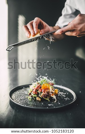 star chef grate cheese on top of fresh food on dark table  Royalty-Free Stock Photo #1052183120