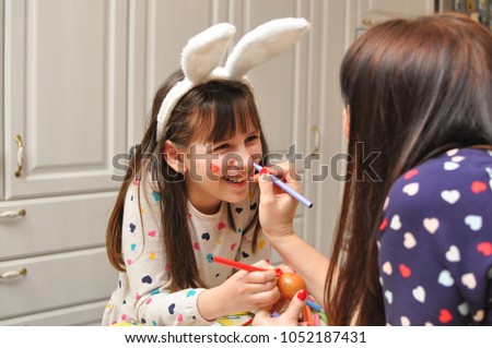 Mom and girl smiling and play with Easter eggs and paint. Mother and daughter painting Easter eggs. Happy family