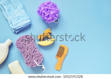 Bathroom items on a blue background. Shampoo, towel, purple sponge, wooden horse toy and hair brush. Flat lay beauty still life photography