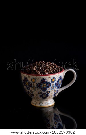 A coffee cup with coffee beans is captured in low light against a black background