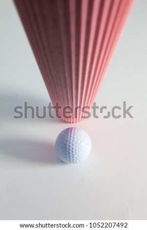 Corrugated pink paper roll and golf ball on the white desk. Exclamation mark.