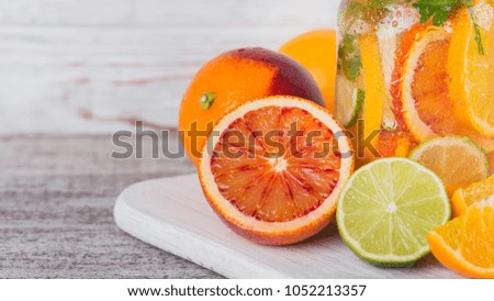 Citrus fruit and herbs water for detox or dieting in glass bottles on wooden board, white background. Limes and oranges. Clean eating, weight loss, healthy lifestyle concept