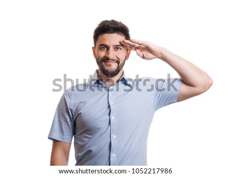 Portrait of handsome man. Young black haired guy with facial hair in blue casual shirt saluting with hand at forehead Royalty-Free Stock Photo #1052217986