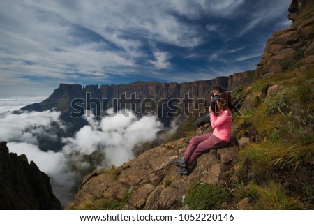 Two photographers photograph the beauty of the Drakensberg Amphitheatre from the Witches Viewpoint in the Ukhahlamba Drakensberg Park, South Africa. A low cloud inversion and high clouds and blue sky. Royalty-Free Stock Photo #1052220146