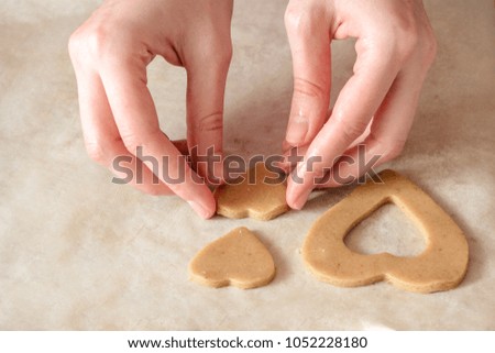 woman with her hands making homemade ginger cookies in the form of hearts on a wooden table.