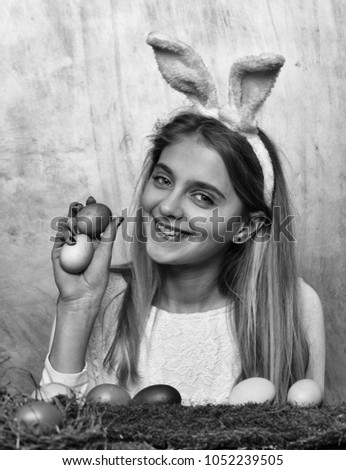 happy easter girl in pink bunny ears with colorful painted eggs, on green moss, has long blonde hair on yellow background. traditional spring holiday celebration