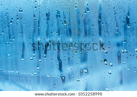 Blue background of natural water condensation, window glass with high air strong humidity, large drops drip. Collecting and streaming down Royalty-Free Stock Photo #1052258990