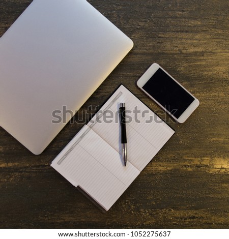Top view of  table or desk with laptop, blank notebook, pen and smart phone on old bronze background with copy space for text.