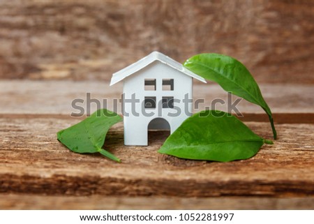 Miniature white toy model house with green leaves on wooden backgdrop. Eco Village, abstract environmental background. Real estate mortgage property insurance dream home ecology concept