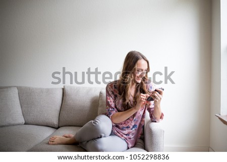 Happy young woman using cell phone at home on couch