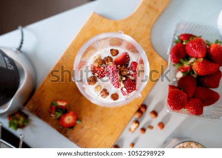 Above view of blender bowl filled with milk fresh strawberries and hazelnuts ready to be made into a smoothie.