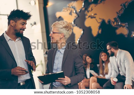 Businessman and businesswoman reviewing contract; business team working in the background. Focus on the man in the foreground Royalty-Free Stock Photo #1052308058