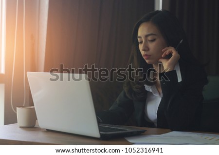 attractive business woman working with thinking and holding pen on table with laptop and coffee cup in officedark tone.