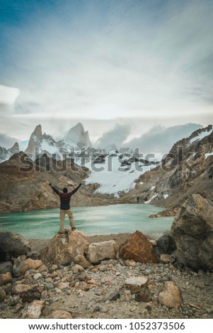 Man super excited in front of the peak of Fitz Roy and amazing laguna. Nice, cold and cloudy day in the national park of El Chalten. 