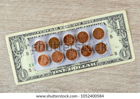 the high cost of medicines: a pack of pills is on the dollar, each tablet is a coin, on wooden background