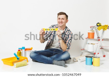 Man in casual clothes sitting on floor with bubble spirit level, instruments for renovation apartment isolated on white background. Wallpaper, gluing accessories, painting tools. Repair home concept