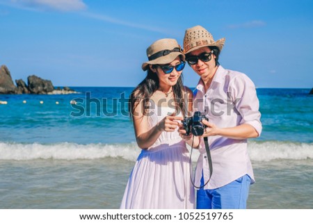 Asia couple love on the beach.a man and a woman looking for picture on camera near the sea on vacation.couple travelers enjoying holiday.