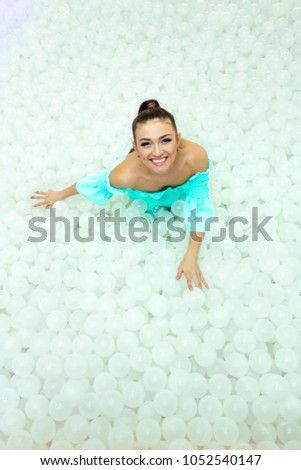 Happy beautiful woman lays surrounded by white plastic balls in the dry pool for adult.