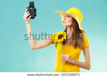 Summer woman wearing yellow dress and hat with sunflower taking self picture with old vintage camera on blue background