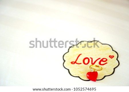 Golden ring with little red heart and paper note “Love” isolated on white background. Surprise gift for special person. Wedding , present concept. Can be use created of any card or banner.