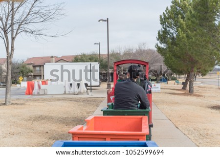 Unidentified kids and parents riding on trackless train ride wagon near local street. Train crossing sign at public park winter event in Irving, Texas, USA