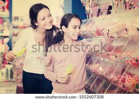 Mother with smiling daughter buying fruit candy in the candy shop