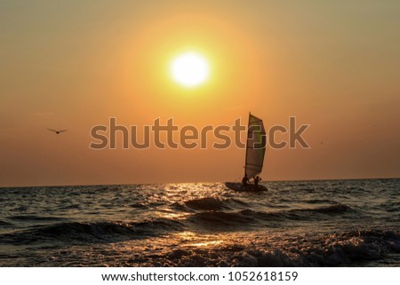 Young couple under sail at sunset. Sailboat with setting sun in the background