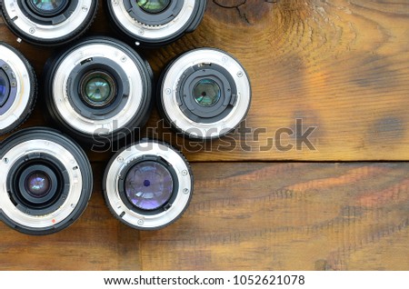 Several photographic lenses lie on a brown wooden background. Space for text