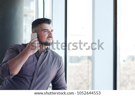 Handsome businessman talking on the phone by the window in his office.