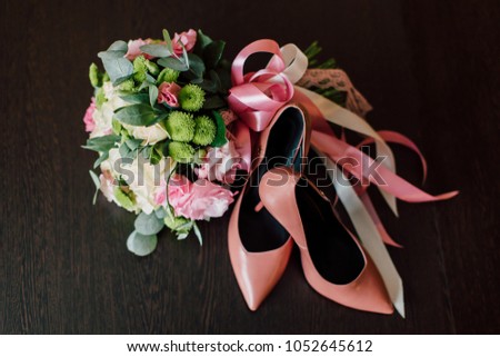 wedding bouquet of fresh flowers with ribbons lies on a dark brown table next to the bride's pink shoes
