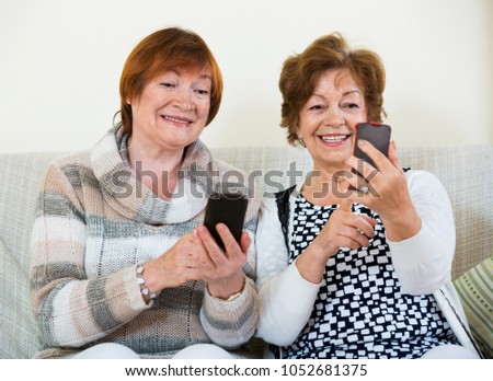 Cheerful satisfied mature women browsing internet on smarthphones indoor Royalty-Free Stock Photo #1052681375