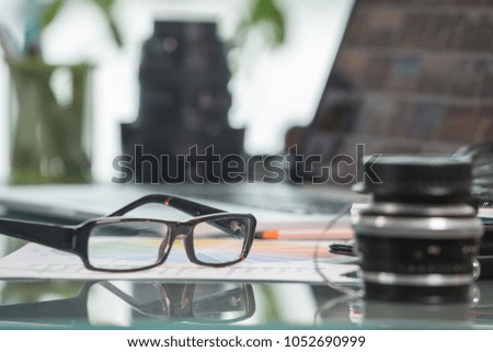 Glasses in focus on a table with laptop and photo lenses out of focus