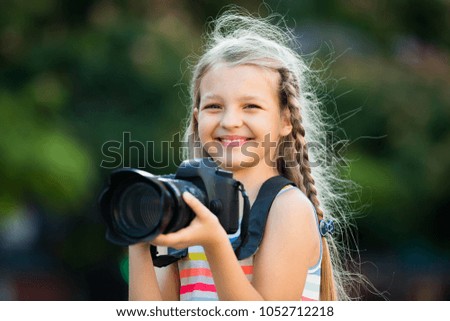 Portrait of cheerful little girl making photo with big camera in hands outdoors
