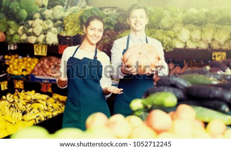 Friendly smiling market stuff offering for retail large squash . Focus on woman
