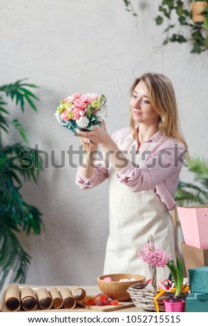 Picture of florist holding bouquet in hands at table with marmalade, marshmallow, boxes, paper