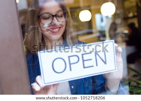 Portrait of beautiful young woman hanging the open sign on a glass door in the store.
