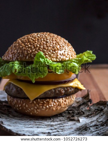 Fresh homemade burger on little wooden cutting board over dark background. Square image with selective focus