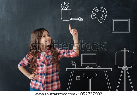 Creative child. Cute happy emotional girl pointing her finger up and talking about famous picture galleries while being at the Art lesson and making an interesting report