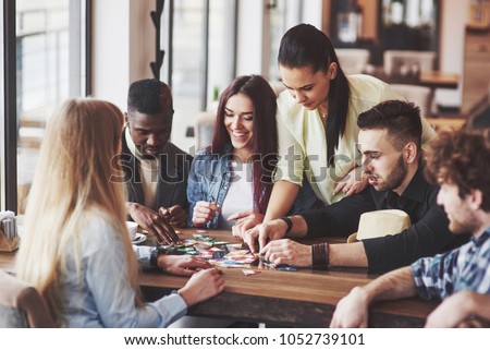 Group of creative friends sitting at wooden table. People having fun while playing board game. Royalty-Free Stock Photo #1052739101