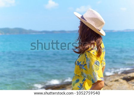 side view of beautiful asian female in fashion yellow shirt stand on the beach looking forward to see amazing blue sky with a little cloud and seascape in a sunny day