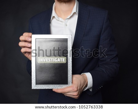 In the hands of a businessman a frame with the inscription:INVESTIGATE