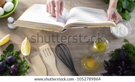 Lady reading pizza recipe in culinary book at home with kitchenware on table Royalty-Free Stock Photo #1052789864