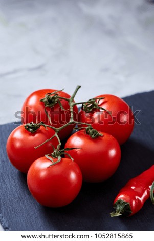 Composition of tomato bunch and sweet pepper on black piece of board, top view, close-up, vertical