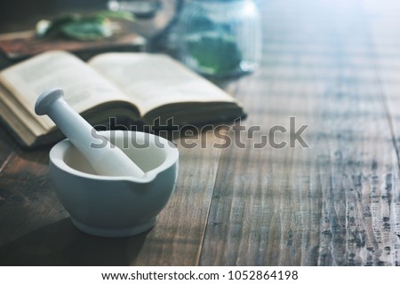 Mortar and pestle with pharmaceutical preparations's book and herbs on a wooden pharmacist table, traditional medicine and pharmacy concept Royalty-Free Stock Photo #1052864198