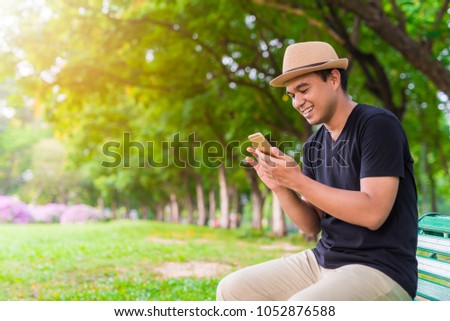 Young asian man using smartphone in park. Royalty-Free Stock Photo #1052876588